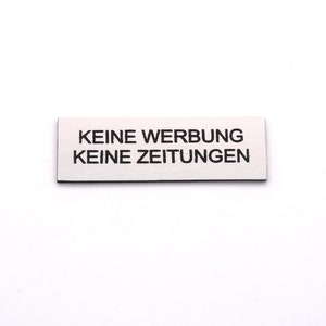 K&ouml;nnte beinhalten: Ein wei&szlig;es rechteckiges Schild mit schwarzem Text, auf dem "KEINE WERBUNG KEINE ZEITUNGEN" steht.
