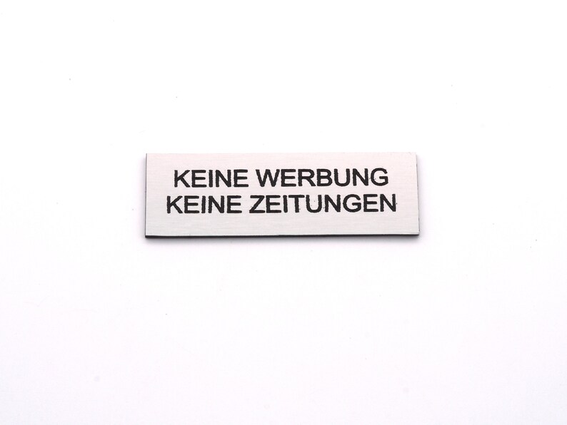 K&ouml;nnte beinhalten: Ein wei&szlig;es rechteckiges Schild mit schwarzem Text, auf dem "KEINE WERBUNG KEINE ZEITUNGEN" steht.