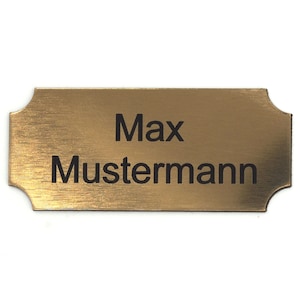 Puede incluir: Una placa de nombre de metal de color dorado con el nombre "Max Mustermann" grabado en letras negras.
