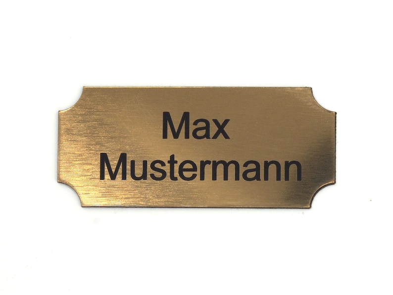 Puede incluir: Una placa de nombre de metal de color dorado con el nombre "Max Mustermann" grabado en letras negras.