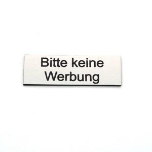 K&ouml;nnte beinhalten: Ein rechteckiges Schild aus Silber mit schwarzem Text, auf dem "Bitte keine Werbung" steht.