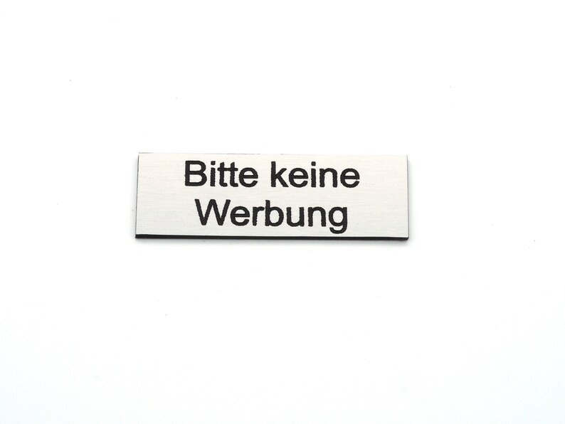 K&ouml;nnte beinhalten: Ein rechteckiges Schild aus Silber mit schwarzem Text, auf dem "Bitte keine Werbung" steht.