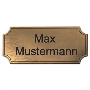 Puede incluir: Una placa de nombre de metal de color dorado con esquinas redondeadas y acabado cepillado. La placa tiene el texto "Max Mustermann" grabado en negro.