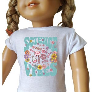 May include: White t-shirt with a blue and green graphic that says "Science Vibes". The graphic includes flowers, a DNA strand, a beaker, and a chalkboard with the equation E=mc².