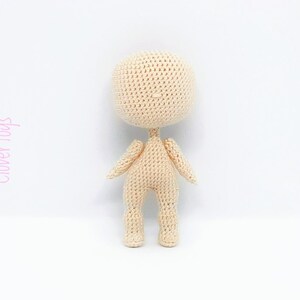 May include: A crocheted doll with a beige body and no facial features. The doll is standing on a white surface.