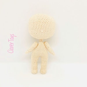 May include: A crocheted doll with a cream-colored body and no facial features. The doll is standing with its arms outstretched.