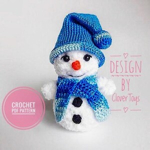 May include: Crochet pattern for a snowman amigurumi toy. The snowman is wearing a blue hat and scarf. The pattern is available as a PDF download. "DESIGN BY Clover Toys" is written on the image.