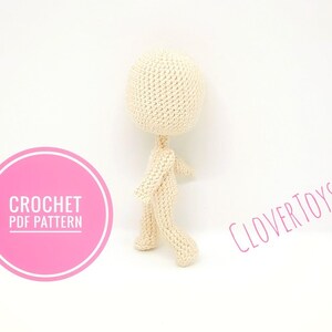 May include: A crochet pattern for a small, beige, amigurumi doll. The pattern is available as a PDF download. The image shows the doll standing on a white background. The text "CROCHET PDF PATTERN" is on a pink circle in the lower left corner of the image. The text "CLOVERTOYS" is in the upper right corner of the image.