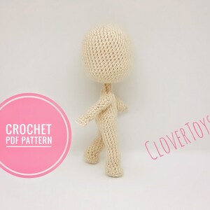 May include: Crochet PDF pattern for a beige amigurumi doll. The doll is standing with its arms outstretched and legs slightly apart. The pattern is available for download from Clover Toys.