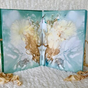 May include: A handmade book with a green cover and delicate floral designs pressed into the pages. The book is tied closed with a brown ribbon.