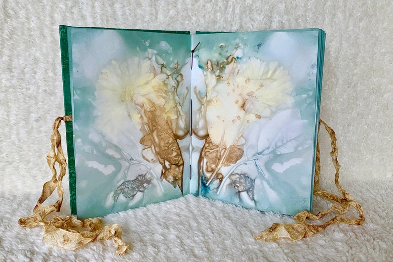May include: A handmade book with a green cover and delicate floral designs pressed into the pages. The book is tied closed with a brown ribbon.