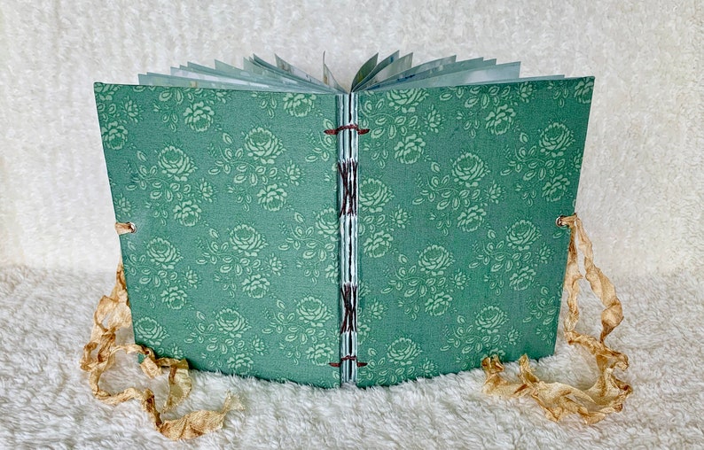 May include: A small, green fabric-covered journal with a floral pattern. The journal is closed and has brown ribbon ties.