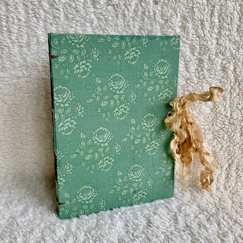 May include: A green fabric-covered journal with a floral pattern and a brown ribbon tied around it.