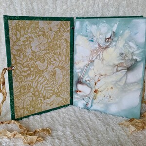 May include: An open book with a green cover and a gold patterned page on the left. The right page has a blue and white abstract design with brown accents.