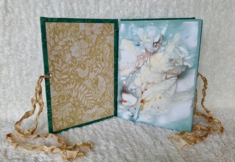 May include: An open book with a green cover and a gold patterned page on the left. The right page has a blue and white abstract design with brown accents.