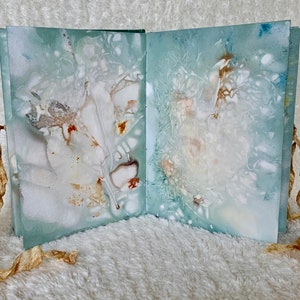 May include: A handmade book with a blue-green cover and white and brown marbling. The book is tied closed with a brown ribbon.