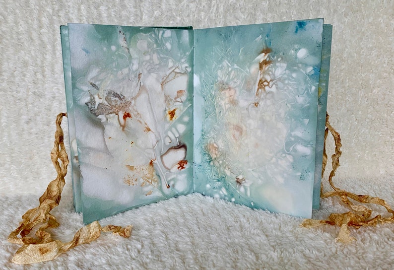 May include: A handmade book with a blue-green cover and white and brown marbling. The book is tied closed with a brown ribbon.