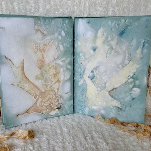 May include: A handmade book with a blue and white marbled cover. The book is open to reveal two pages with pressed leaves and flowers. The book is tied together with a brown ribbon.