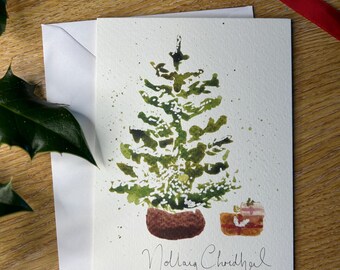 Può includere: Biglietto di Natale ad acquerello con un albero di Natale verde in un vaso marrone e un piccolo cofanetto regalo. Il biglietto è su una busta bianca, con un nastro rosso e foglie verdi sullo sfondo. Il testo "Nollaig Chridheil" è scritto sul biglietto.