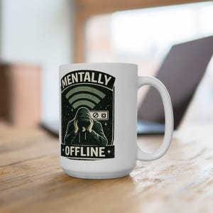 Può includere: Tazza in ceramica bianca con grafica nera e verde. La grafica presenta una persona con una felpa con cappuccio con le parole "MENTALLY" sopra e "OFFLINE" sotto. Un simbolo wifi e uno schermo di computer sono anch'essi nel design.