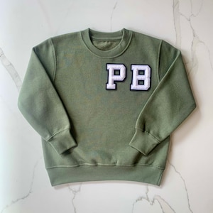 May include: A green sweatshirt with a white felt patch that says "PB" in a varsity style font.