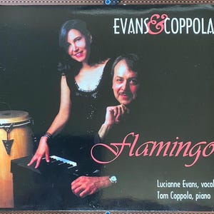 May include: A black and white album cover with a pink title that reads "Flamingo". Two musicians, a woman and a man, are pictured. The woman is wearing a black dress and the man is wearing a black shirt. The album cover also includes the text "Evans & Coppola" and the names of the musicians, "Lucianne Evans, vocals" and "Tom Coppola, piano".