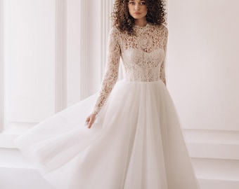 May include: A white lace and tulle wedding dress with long sleeves and a high neckline. The dress has a fitted bodice and a full skirt.