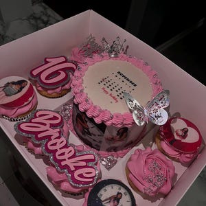 May include: A pink birthday cake and cupcakes in a box. The cake has a photo print and a butterfly decoration. Cupcakes are decorated with pink frosting, the number 16, and the name "Brooke".