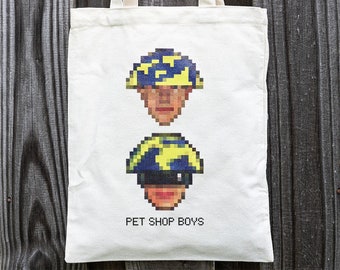 May include: A white canvas tote bag with a pixelated image of two men wearing yellow and blue hats. The text "PET SHOP BOYS" is printed below the images.