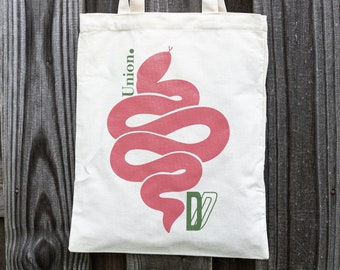 May include: A white canvas tote bag with a pink snake design and the word "Union." printed in green on the front.