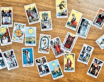May include: A collection of twenty-two rectangular tarot cards scattered across a surface. Each card features distinct colorful illustrations and specific titles such as The Sun, The Moon, The Empress, The Chariot, The Fool, Strength, The Emperor, The World, The Hierophant, Justice, The Hanged Man, Temperance, Judgement, The Hermit, The Tower, The Star, The Magician, Death, and The Devil.