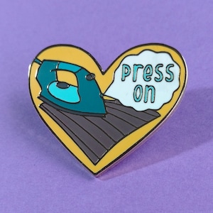 Puede incluir: Un pin de esmalte en forma de corazón amarillo con una plancha azul y una burbuja de diálogo blanca que dice "press on".