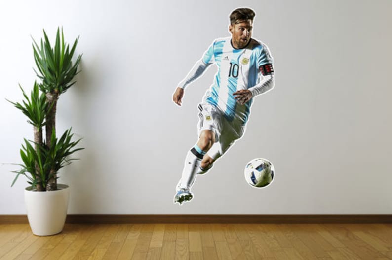 May include: A soccer player in a light blue and white jersey with the number 10 on the front, dribbling a soccer ball. The player is wearing white shorts and black socks. The background is a white wall.