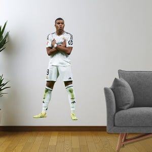 May include: A football player wearing a white jersey with black accents and black shorts. The player is standing with their arms crossed and is wearing white socks and yellow boots. The player is wearing a number 9 on their jersey.