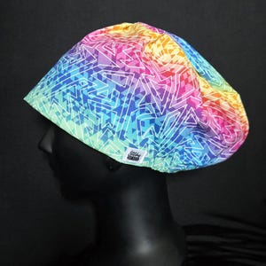 May include: A colorful, patterned hat with a geometric design. The hat features a vibrant mix of colors, including pink, blue, yellow, and green, with white lines. The hat is worn by a mannequin head.