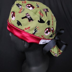 May include: Green scrub hat with a red satin band and a black bow. The hat features a repeating pattern of Freddy Krueger's glove, a street sign that says "Elm St", and a silhouette of Freddy Krueger's head.