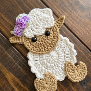 May include: A crocheted white lamb with brown legs and a purple flower crown.