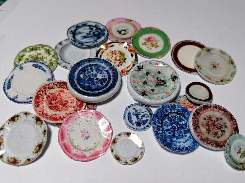 Op de afbeelding: Een verzameling miniatuur keramische borden met verschillende bloem- en geometrische patronen in tinten blauw, groen, rood, roze en wit.
