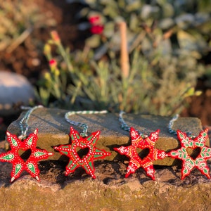 May include: Four red wooden star ornaments with green and white painted details. Each star has a heart-shaped cutout in the center and is attached to a white and green string.