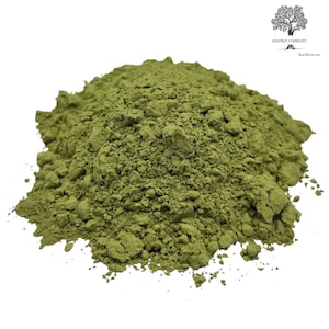 Puede incluir: Un montón de polvo fino de color verde oliva con una consistencia texturizada y grumosa. La sustancia está apilada en un montículo sobre un fondo blanco liso. En la esquina superior derecha, un pequeño logotipo negro muestra un árbol y el texto AGORA MARKET.