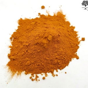 Puede incluir: Primer plano de un montón de polvo de cúrcuma de color naranja brillante sobre un fondo blanco.