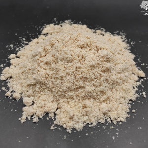 May include: A close-up of a pile of light brown almond flour on a black surface.