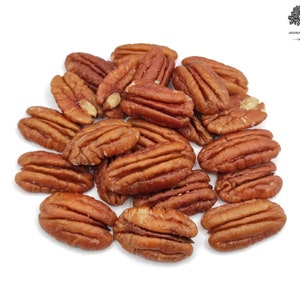 Può includere: Primo piano di un mucchio di metà noci pecan. Le noci pecan sono di colore marrone chiaro e hanno una consistenza leggermente ruvida. Sono disposte in uno schema casuale.