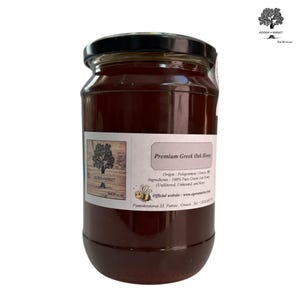 以下が含まれることがあります： 白いラベルに「Premium Greek Oak Honey」と書いてある、濃い琥珀色の蜂蜜が入ったガラス瓶。ラベルには産地、原材料、ウェブサイトの情報も記載されています。瓶は白い背景の上に置かれています。