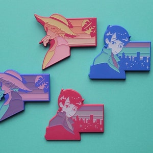 Op de afbeelding: Set van vier emaillepins met kleurrijke illustraties van mensen met stadsgezichten op de achtergrond. De pins zijn in tinten blauw, roze en rood.