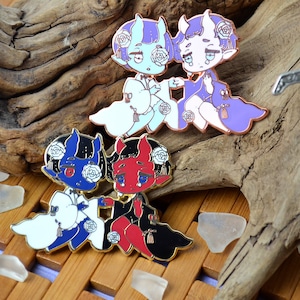 Op de afbeelding: Vier emaillepins met cartoonfiguren met hoorns en witte rozen. De figuren zijn in verschillende poses en kleuren, waaronder blauw, rood en paars.