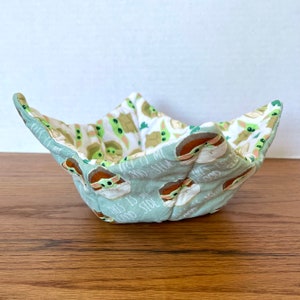 May include: A green and white fabric bowl with a pattern of Baby Yoda characters. The bowl has the text "This is my good side" on it.