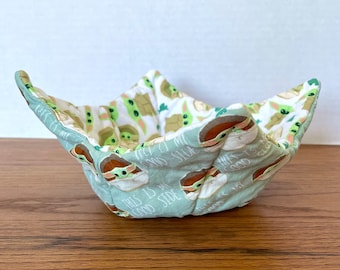 May include: A green and white fabric bowl with a pattern of Baby Yoda characters. The bowl has the text "This is my good side" on it.