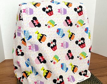 May include: White appliance cover with a colorful pattern of Mickey Mouse heads wearing cupcake hats. The cupcakes are decorated with sprinkles and have different colored frosting. The cover has a black handle.