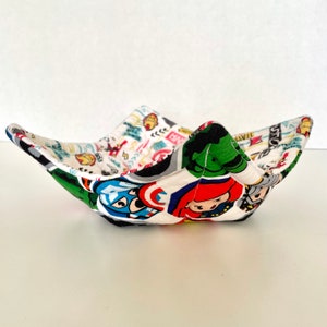 May include: A white fabric bowl with a colorful print of superheroes, including Captain America, Hulk, Iron Man, and Thor. The bowl is folded and has a quilted texture.